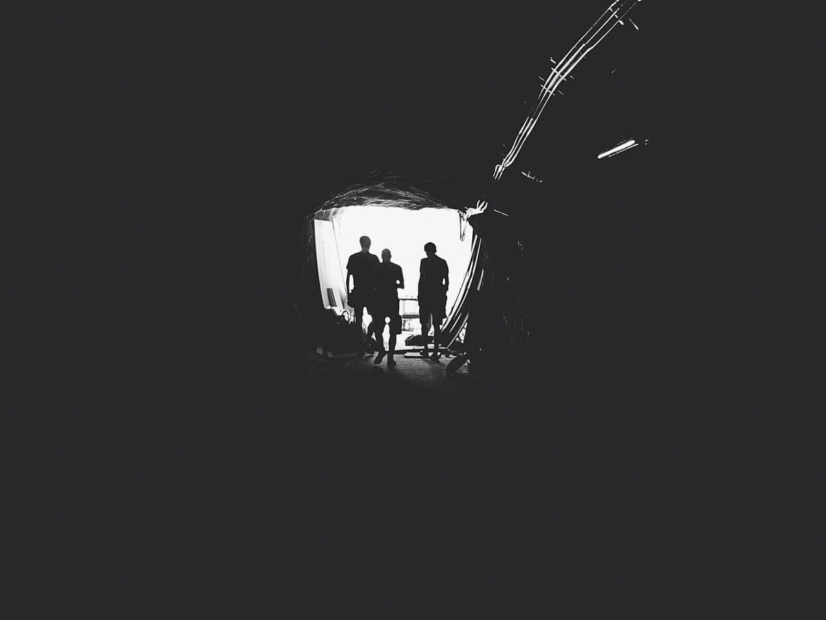 Figures silhouetted in a dark tunnel beneath a single light